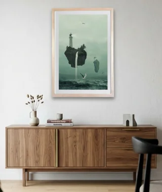 Framed surreal floating island artwork with a lighthouse above a wooden sideboard