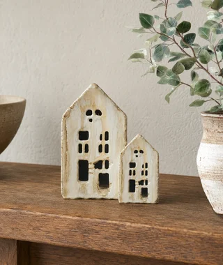 Two small ceramic house sculptures displayed on a wooden shelf